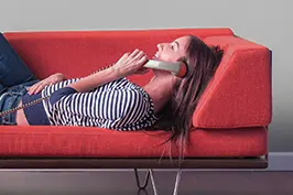 Uma moça deitada em um sofá vermelho sorrindo com um telefone no ouvido.